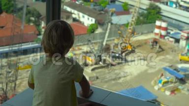 <strong>一个小</strong>男孩坐在有<strong>玻璃</strong>墙的阳台上，看着一栋多层建筑的建造